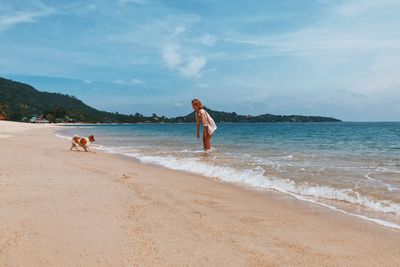Woman playing with dog on beach against sky