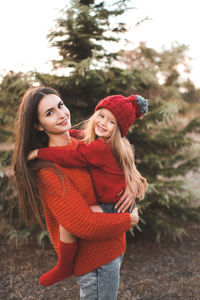 Young woman mom spend time with daughter kid girl wear red knit sweater and hat over tree outdoor