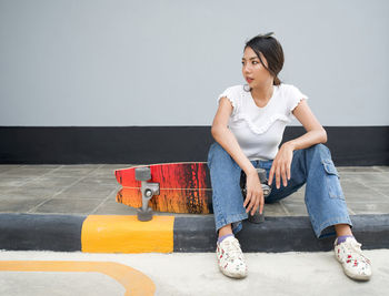 Young woman looking away while sitting on wall