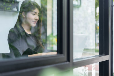 Businesswoman using laptop while sitting in office seen through window
