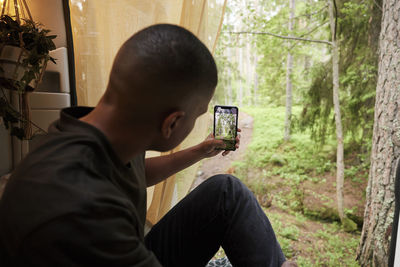 Man sitting in camper van and photographing forest