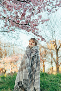 Portrait of a little boy wrapped in a blanket enjoying cherry blossoms in a city park.