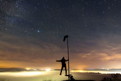 Silhouette man standing on pole against sky at night