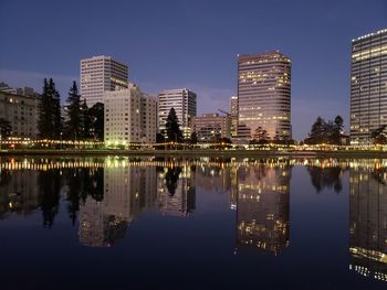 Reflection of illuminated buildings in lake against clear sky at night