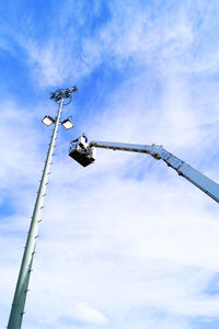 Low angle view of man standing on cherry picker by floodlight against sky