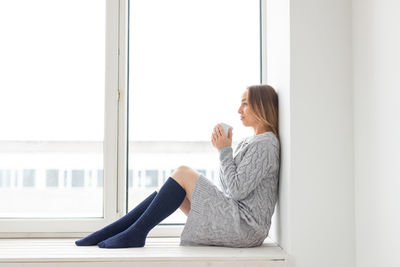 Side view of woman sitting on window at home