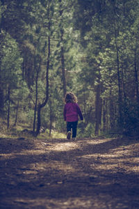 Rear view of woman walking on road in forest