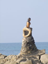 Statue on rock by sea against clear sky