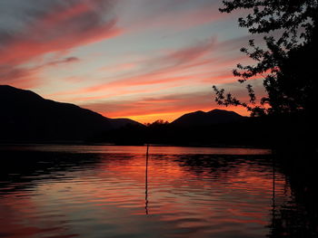 Scenic view of lake by silhouette mountains against romantic sky at sunset