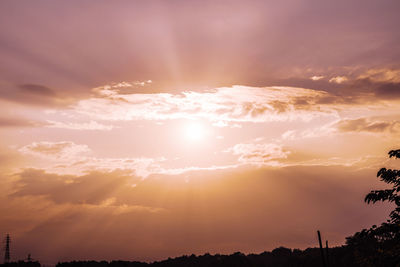 Low angle view of sun streaming through clouds during sunset