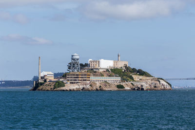 Lighthouse amidst buildings by sea against sky