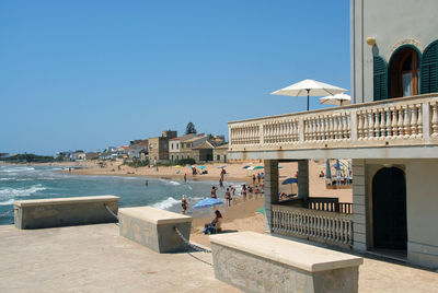 People by buildings against clear blue sky