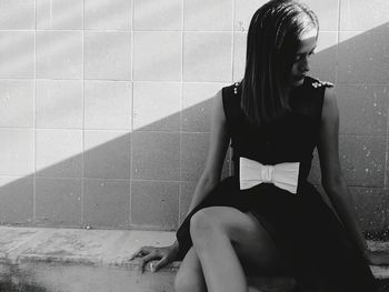 Girl sitting against wall on sunny day