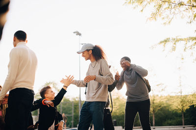 Happy friends greeting each other at skateboard park against clear sky