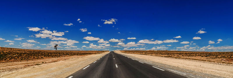 Road leading towards desert against blue sky