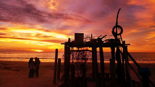 Silhouette people on beach against sky during sunset