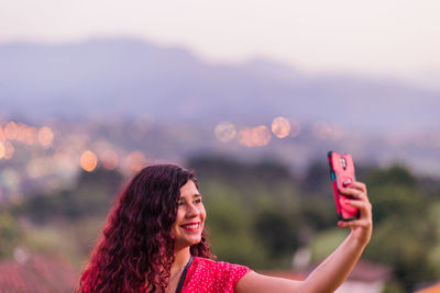Side view of woman using mobile phone against sky during sunset