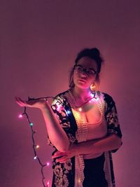 Portrait of young woman standing against illuminated background