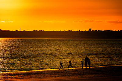 Silhouette people on beach against sky during sunset