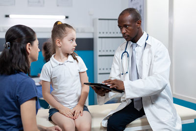 Doctor examining girl sitting on bed at hospital