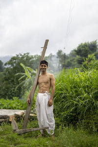 Happy indian farmer standing with wooden plough in rice field