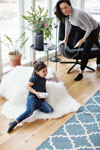 Mother listening music through mobile phone while daughter leaning on fake fur at home