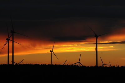 Silhouette wind turbines on field against sky during sunset