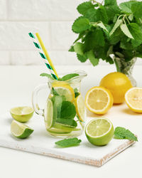 Transparent glass decanter with slices of lemon, lime and mint leaves on a white table, 