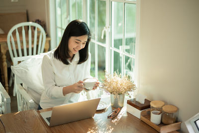 Young businesswoman drinking coffee while sitting by window at cafe