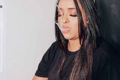 Young woman emitting smoke against wall