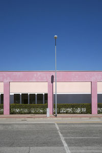 Empty street by building against clear blue sky