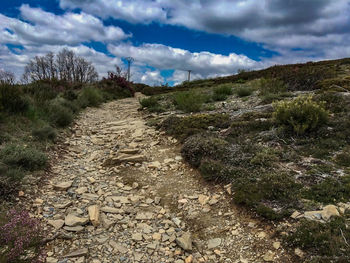 Dirt road passing through landscape against cloudy sky