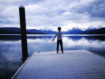 Full length of boy standing on pier by lake against sky