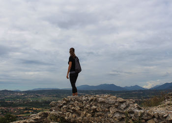 Side view of woman standing on mountain against cloudy sky