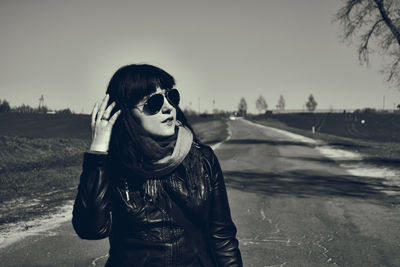 Young woman standing on country road while wearing sunglasses during sunny day