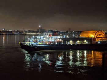 Illuminated city by sea against sky at night