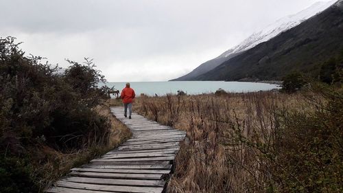 Rear view of woman walking on boardwalk against lake