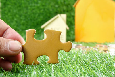 Cropped hand holding jigsaw piece against model house on field