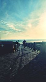 Silhouette man on jetty at beach against sky during sunset