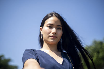 Low angle portrait of young woman against clear blue sky