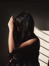 Woman with long hair sitting by wall at home