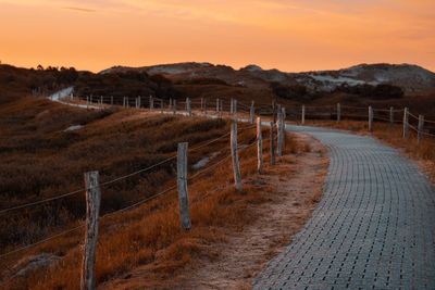 Footpath amidst field against sky during sunset