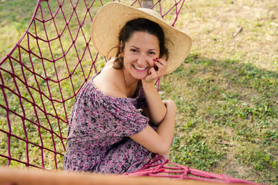 Portrait of smiling young woman sitting on hammock over grass