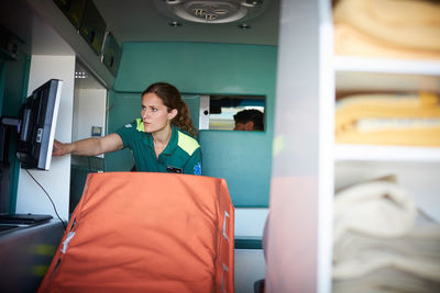 Female paramedic reading monitoring equipment screen in ambulance