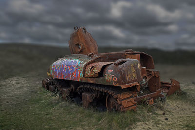 Old rusty wheel on field against sky