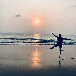 Silhouette woman enjoying on shore at beach against sky during sunset