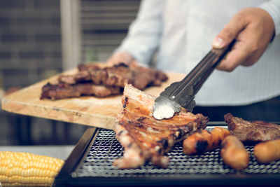 Midsection of man preparing meat on barbecue grill