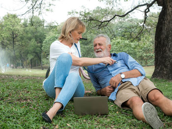 Man and woman using mobile phone while sitting on tree