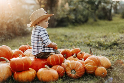 A boy in a cowboy hat and a plaid shirt sits on bright orange pumpkins, side view. holiday