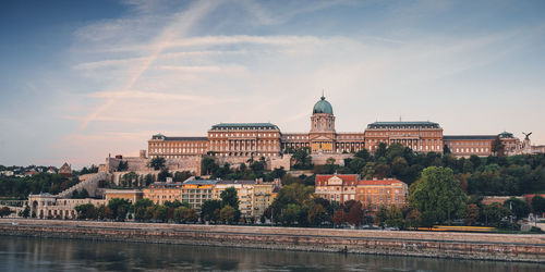 Buildings at waterfront against cloudy sky